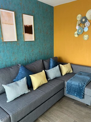 Ein modernes Wohnzimmer mit einem grauen Ecksofa, mehreren Kissen und einer blauen Decke.