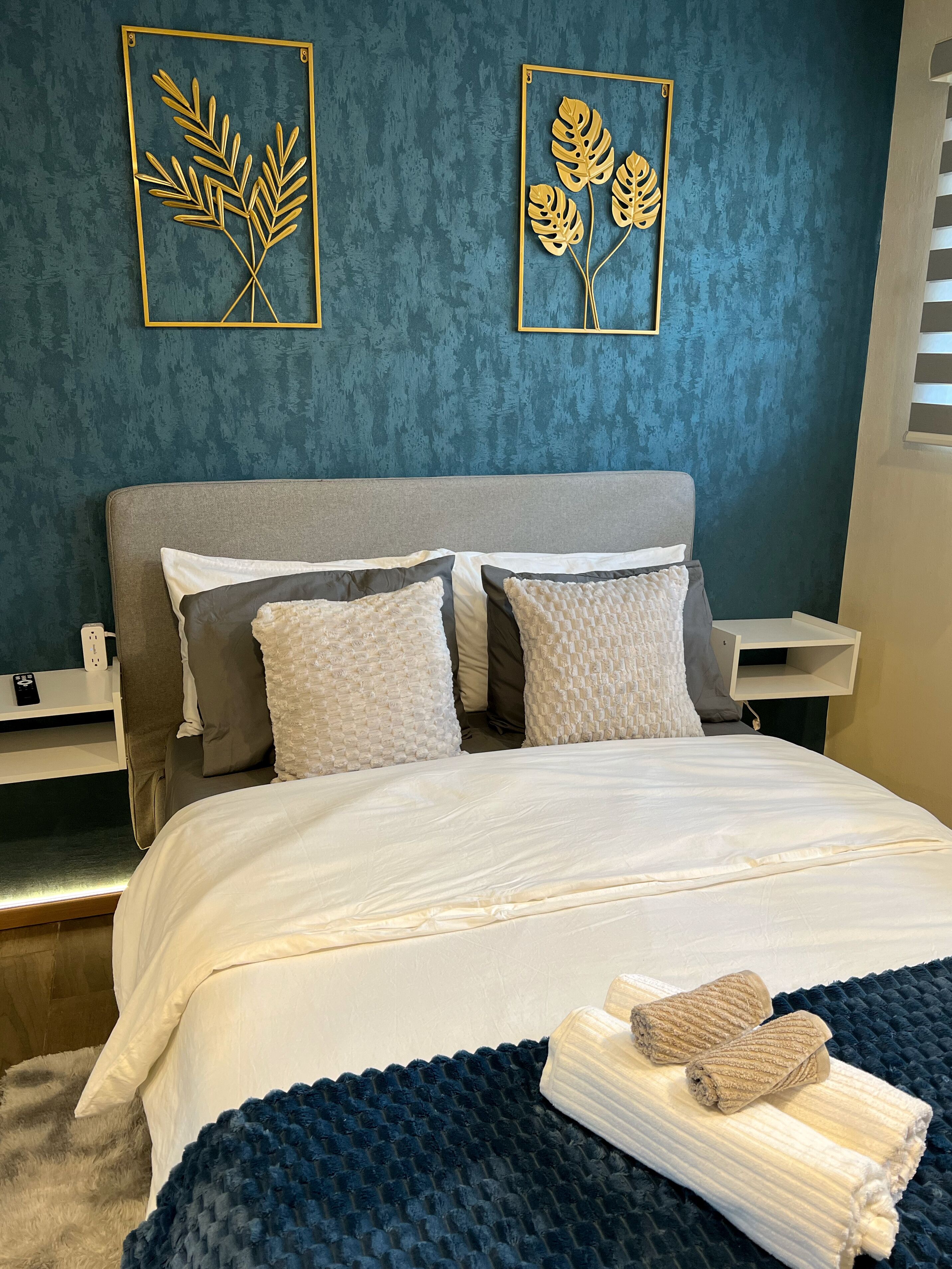 A neatly made bed with white linens, a dark blue textured blanket, and a folded towel on the side.