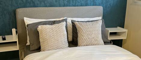 A neatly made bed with white linens, a dark blue textured blanket, and a folded towel on the side.