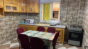 A compact kitchen with wooden cabinets, a microwave, a gas stove, and a dining table with chairs. - Apartment Aloue for a better stay with us welcome (Café chergui)