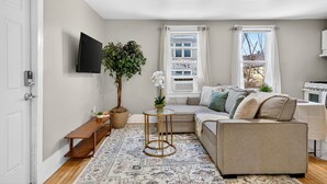 A living room with a sofa, a coffee table, a potted plant, and a television. - Brady St Base, 2BR Flat, Comfortably Sleeps 5 (Milwaukee)