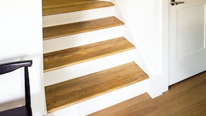 A staircase with wooden steps and a wooden handrail, leading to a white door.