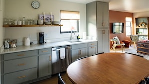 A modern kitchen with grey cabinets, a wooden dining table, and a coffee station.