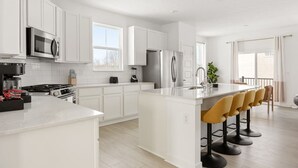 Uma cozinha moderna com armários brancos, eletrodomésticos de aço inoxidável e uma ilha central com banquetas.