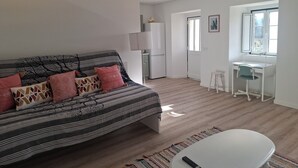 Una sala moderna con sofá, una mesita, un escritorio y un refrigerador.