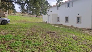 Un edificio blanco con techo de tejas rojas, camino de entrada pavimentado y jardín con césped.