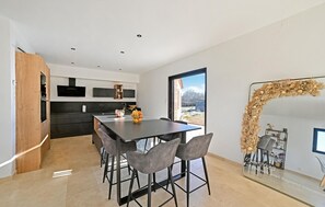 Eine moderne Küche mit Essbereich, ausgestattet mit einer großen Kochinsel, Barhocker und Blick durch eine Glastür.