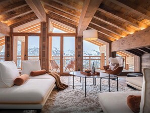 A cozy, wooden-floored living room with a white sofa, a fluffy rug, and a view of snowy mountains through large windows. - Chalet Celestia - Wellness break at the foot of the slopes - OVO Network (Les Belleville)