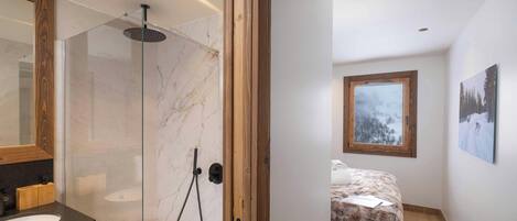 A modern bathroom with a glass-enclosed shower, a wooden vanity, and a marble backsplash.