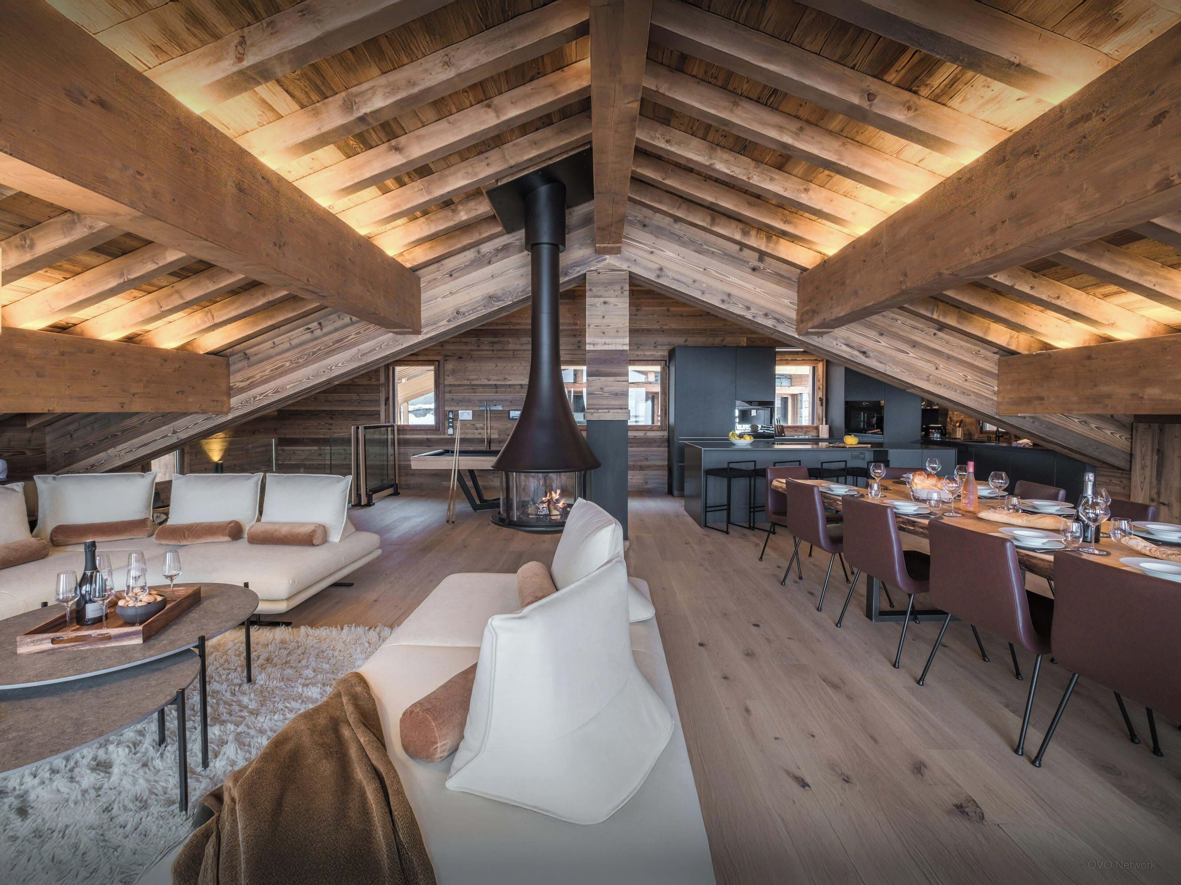 Un loft spacieux avec de hauts plafonds, des poutres apparentes, une cheminée, un coin repas et une cuisine.