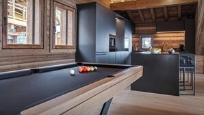 Ein Billardtisch mit Kugeln, Holzwände und eine Küchenzeile mit einem Fenster.