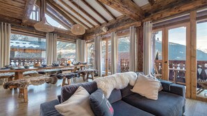 A wooden interior with a sofa, fur throw, and a dining area with a view of mountains.