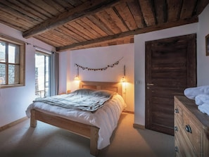 Ein Schlafzimmer mit einem hölzernen Bett, zwei Nachttischlampen, einer Holztür und einem Fenster mit Vorhängen.