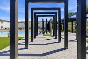 A courtyard with a geometric metal structure, a swimming pool, and a building in the background. - SUPER Cozy Townhome w/ Themed Rooms | Near Disney (3252) (Kissimmee)