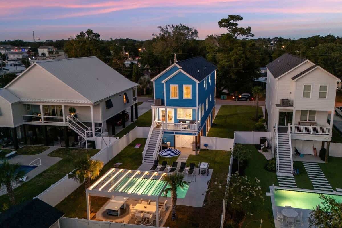 Una casa de dos pisos con fachada azul, un porche delantero y un patio trasero con piscina.