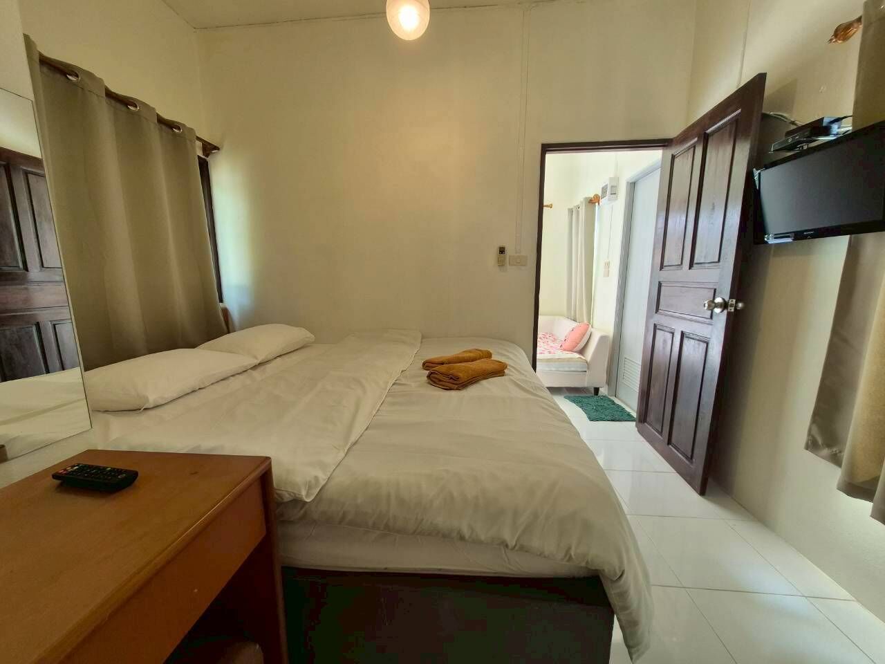 A hotel room with a bed, a wooden nightstand, a television mounted on the wall, and a door leading to another room.