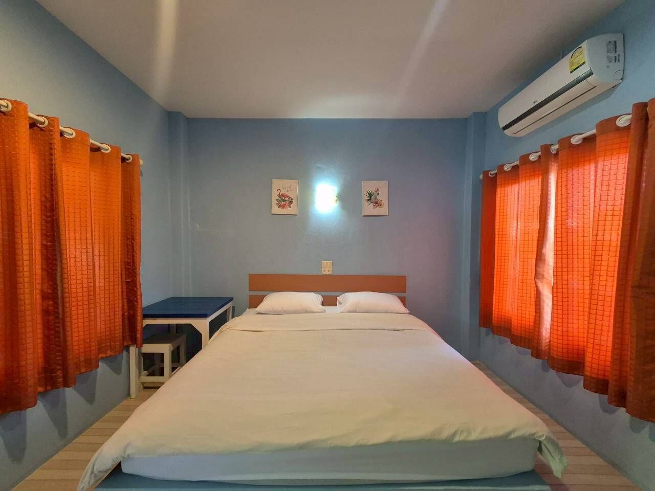 Un dormitorio con cama, dos almohadas, una mesita de noche, un equipo de aire acondicionado y dos cuadros en la pared.