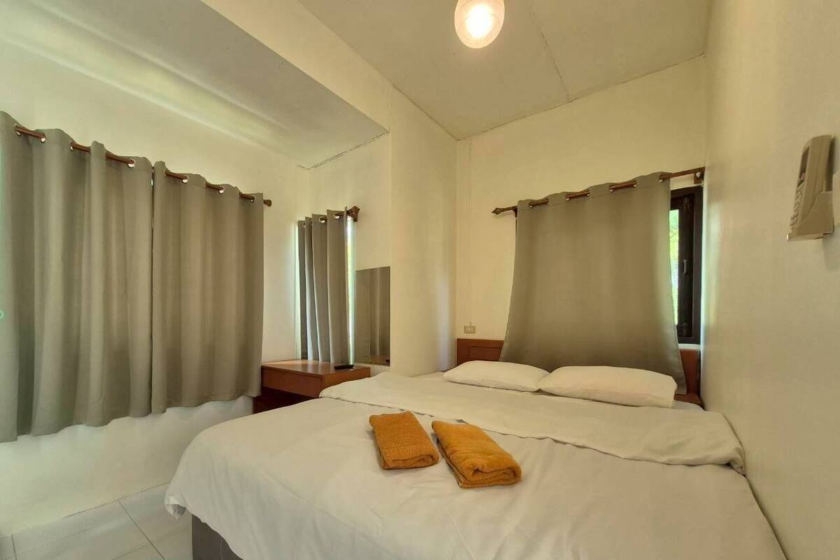 Ein Hotelzimmer mit zwei Betten, einem Nachttisch und einem Fenster mit Vorhängen.