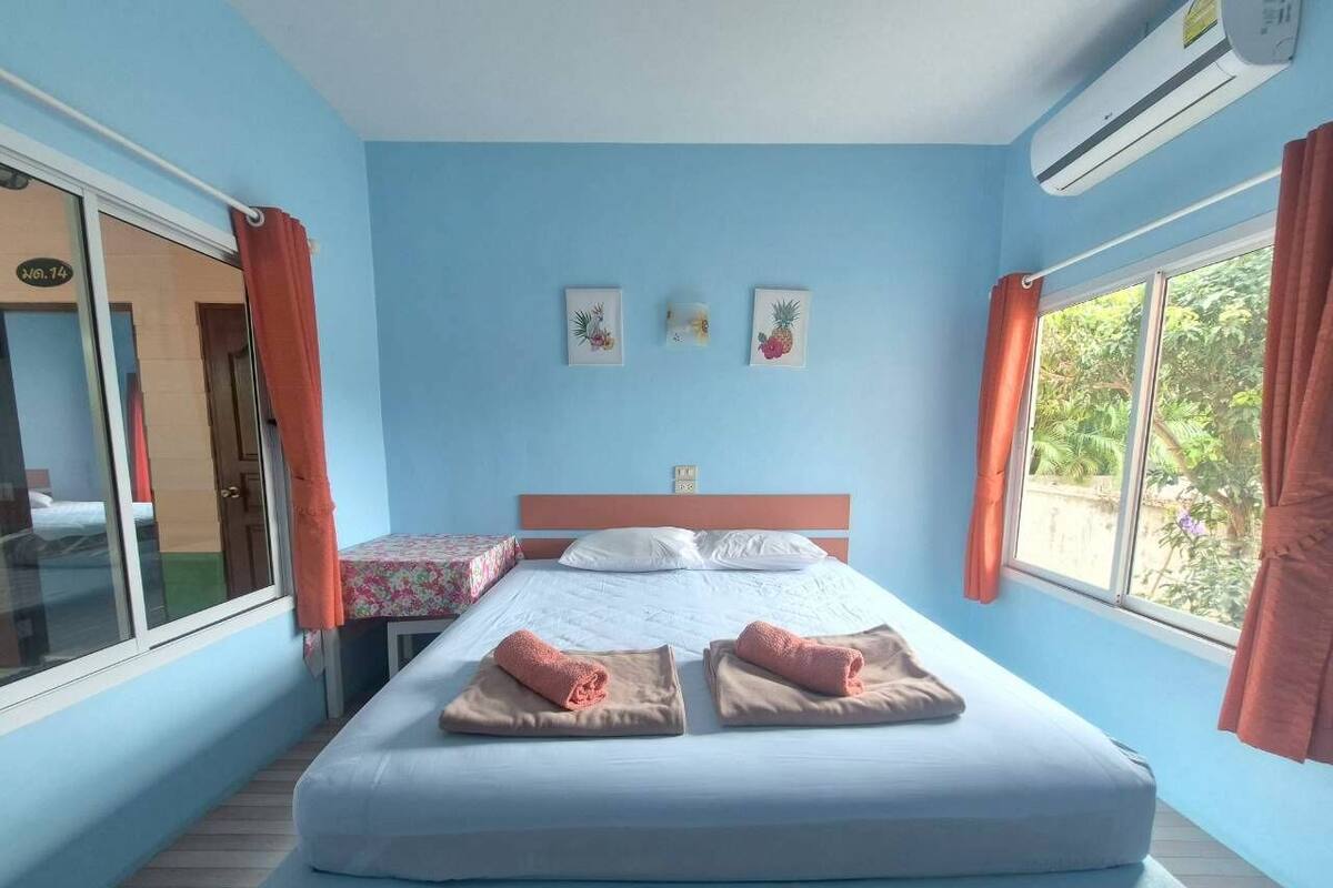 Ein Zimmer mit einem großen Bett, zwei Nachttischen, einem fensterbelaubten Fenster und einer wandmontierten Klimaanlage.