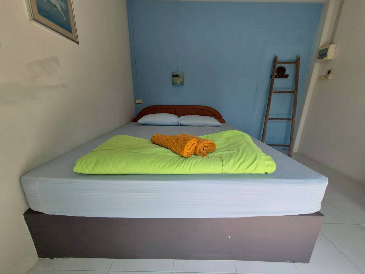 A bed with a green pillow and an orange towel, a wooden ladder, and a blue wall.