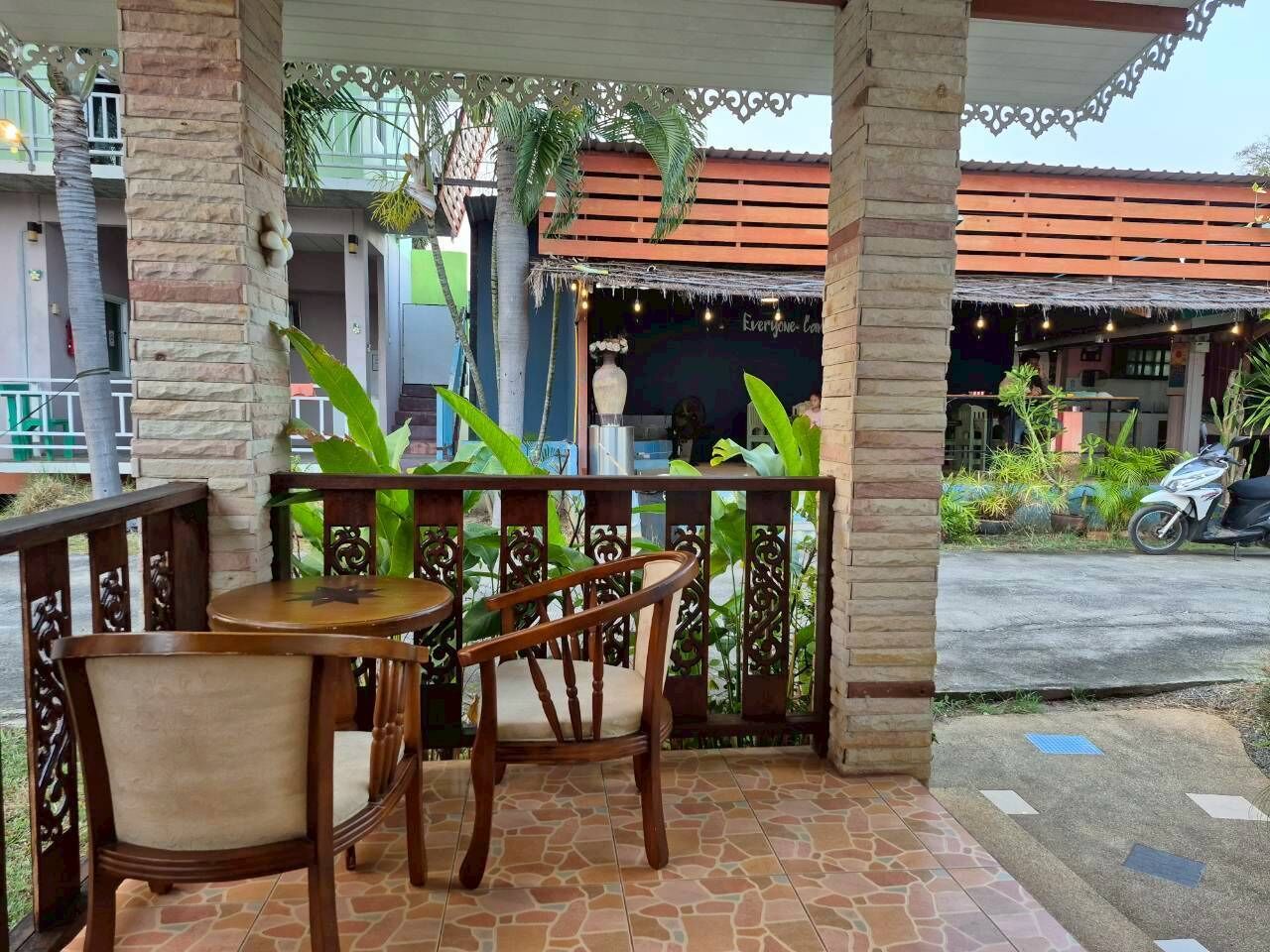A covered outdoor seating area with two wooden tables and chairs, surrounded by a decorative fence and plants.