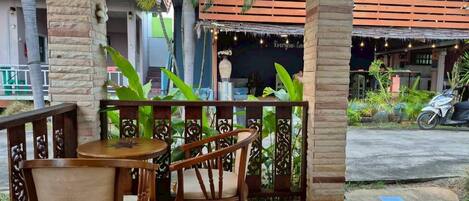 A covered outdoor seating area with two wooden tables and chairs, surrounded by a decorative fence and plants.