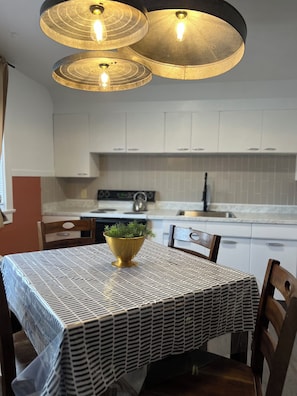 Un área de comedor con una mesa cubierta por un mantel estampado, un cuenco dorado con follaje y una lámpara colgante moderna.