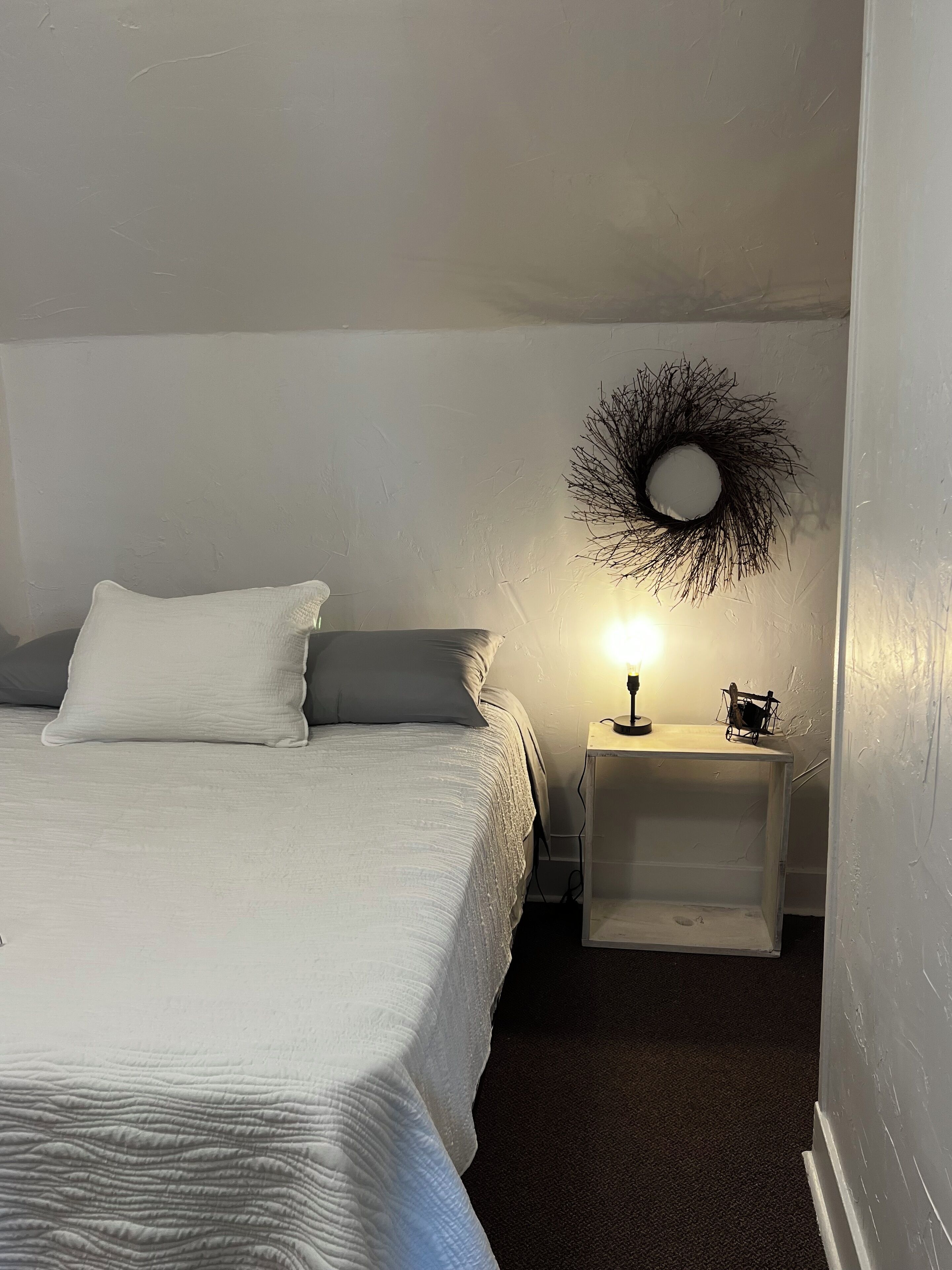 Un dormitorio con cama, mesita de noche con lámpara y espejo en la pared.