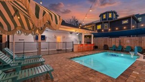 A pool area with lounge chairs, a bar, and a building with a tower.