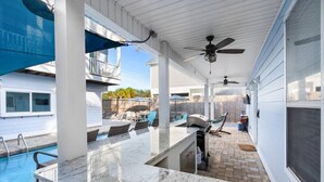 A covered outdoor area with a pool, seating, and a ceiling fan.