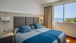 Ett hotellrum med en stor säng, två sängbord, ett litet bord, ett fönster med utsikt över havet och en gardin.