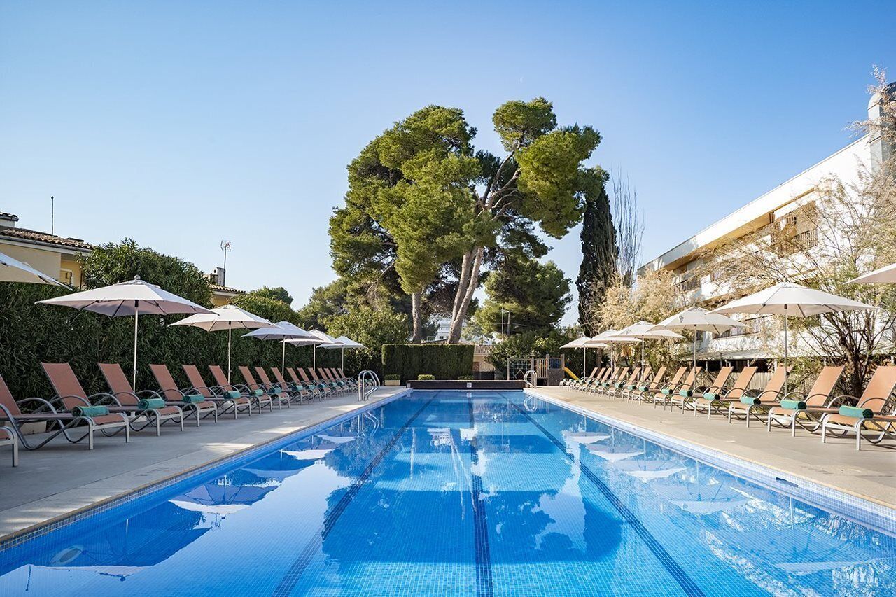 Una piscina amb gandules i ombrel·les, envoltada d'arbres i edificis.
