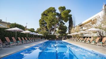 Una piscina amb gandules i ombrel·les, envoltada d'arbres i edificis.