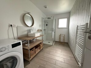 Une salle de bain moderne équipée d’un lave-linge, d’un meuble-lavabo en bois, d’une cabine de douche en verre et d’un radiateur.