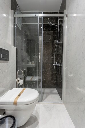 A modern bathroom with a glass-enclosed shower, a white toilet with a beige towel, and marble walls. - New Eco Flat near Cevahir Mall, Şişli (ist)