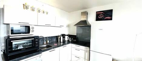 Una cocina compacta con armarios blancos, un microondas Bosch, un horno tostador Bosch, un lavamanos y un refrigerador Bosch.