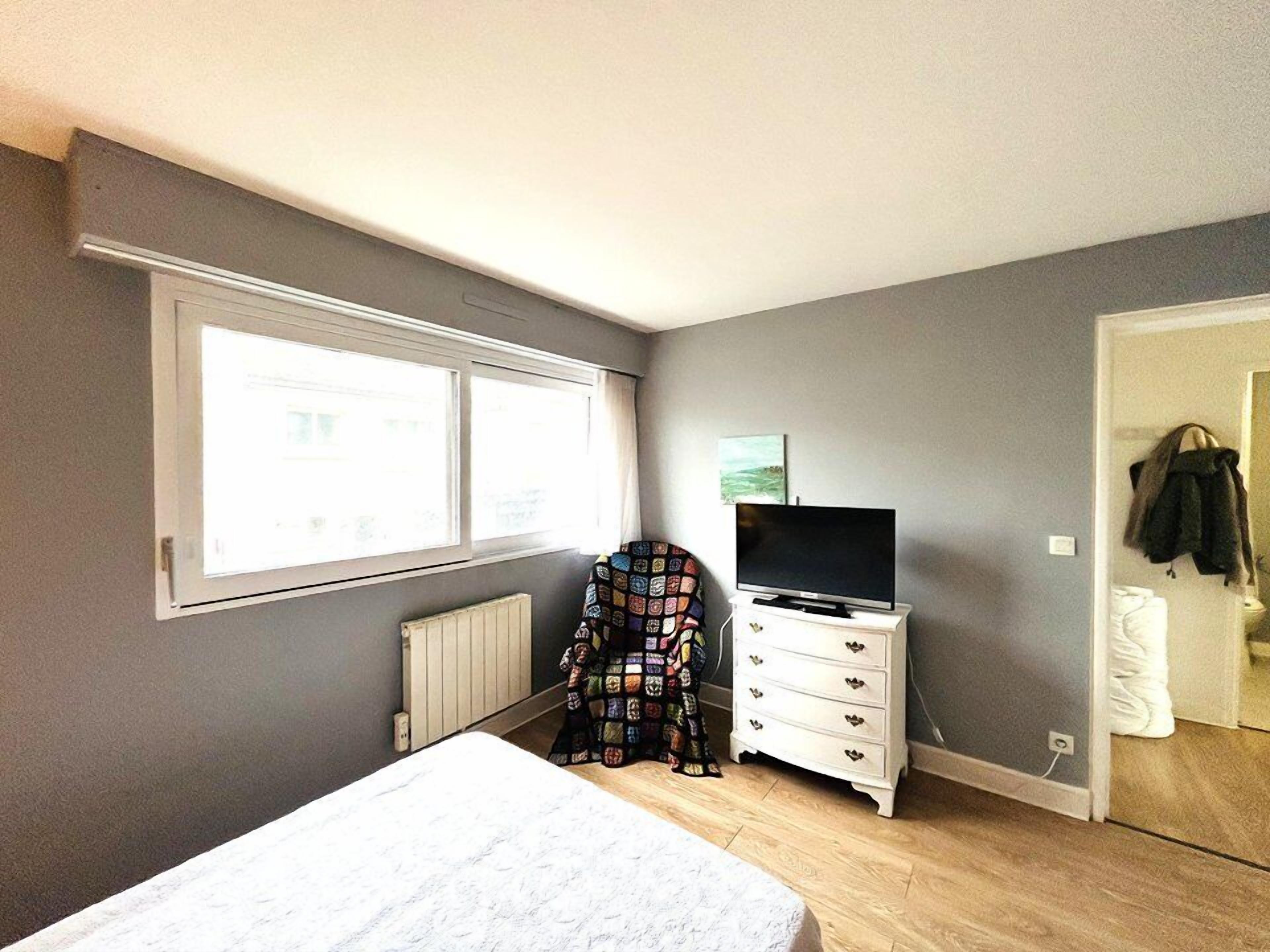A bedroom with a bed, a dresser, a television, and a window.