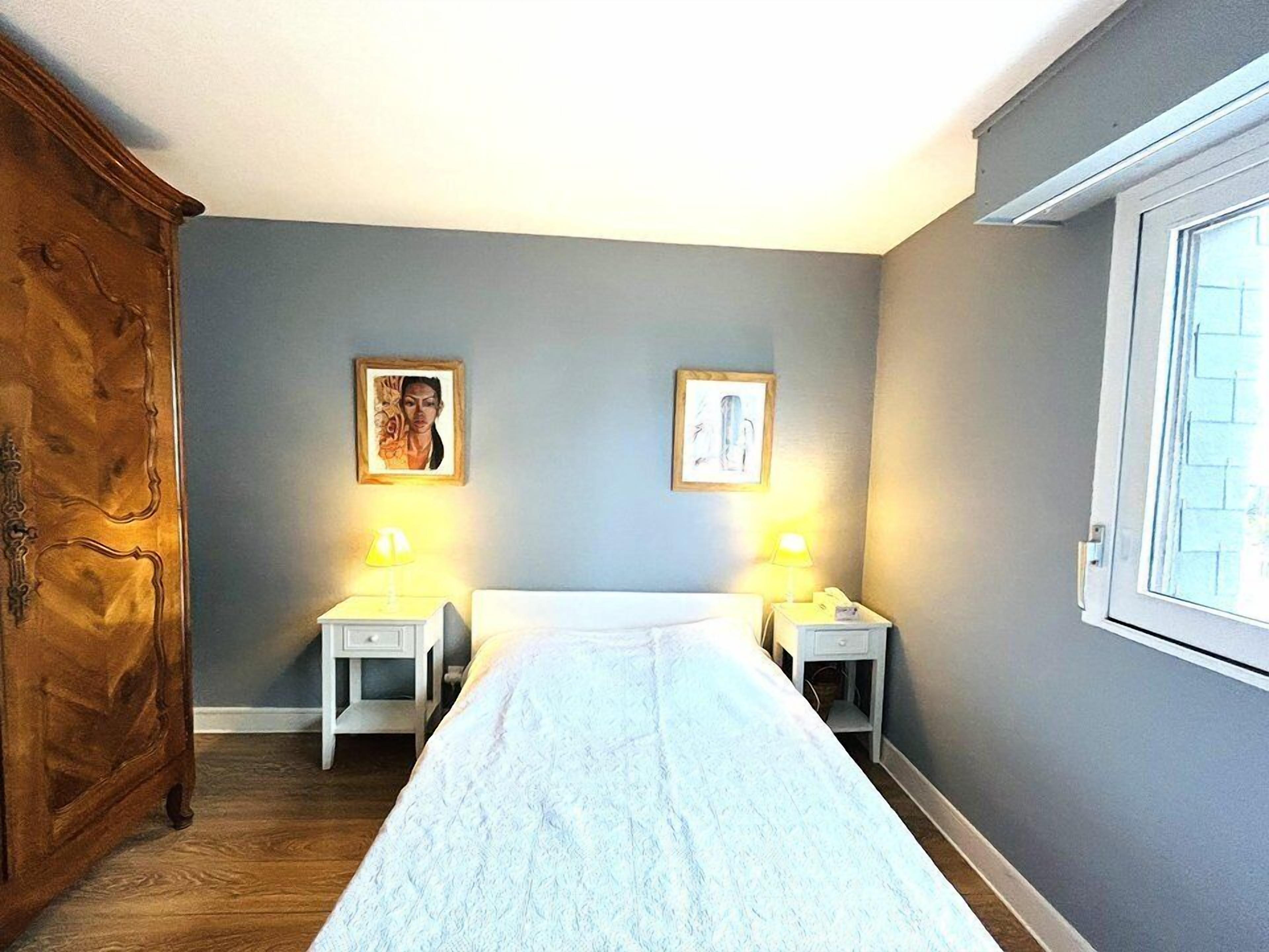 A bedroom with a bed, two bedside tables, a wooden wardrobe, and two wall-mounted paintings.