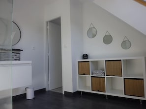 Um interior moderno com uma mesa de consola branca, uma estante branca com cestos e uma porta que dá para outro quarto.