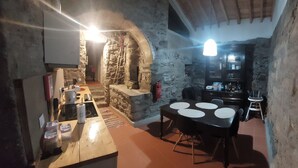 Una habitación rústica con paredes de piedra, una mesa y sillas de madera, una pequeña zona de cocina y un armario de madera oscura.