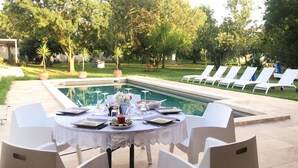 An outdoor dining area with a pool, white chairs, and a table set for a meal. - Gîte dans Mas proche Alpilles (Saint-Martin-de-Crau)