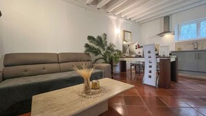 A modern living room with a sofa, a coffee table with decorative items, a dining area with chairs, and a kitchen with a countertop and cabinets. - Gîte dans Mas proche Alpilles (Saint-Martin-de-Crau)