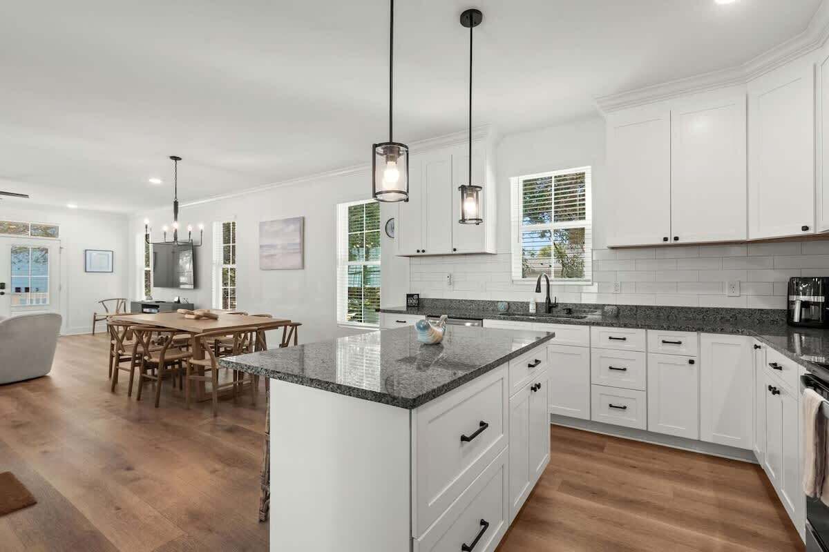 A modern kitchen with white cabinets, granite countertops, and a dining area with wooden chairs.