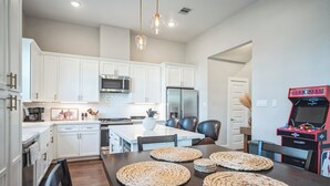 A modern kitchen with white cabinets, a stainless steel refrigerator, and a microwave. There is a dining table with woven placemats and chairs. - 3-bedroom house in nice Houston with cool AC for relaxing stay (Houston)