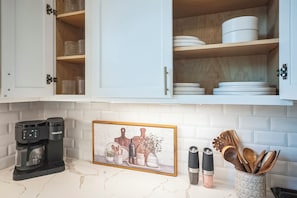 A kitchen with white cabinets, a coffee maker, a framed picture, and kitchen utensils. - 3-bedroom house in nice Houston with cool AC for relaxing stay (Houston)