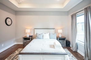 A bedroom with a large bed, two bedside tables with lamps, a wall clock, and a window with curtains. - 3-bedroom house in nice Houston with cool AC for relaxing stay (Houston)