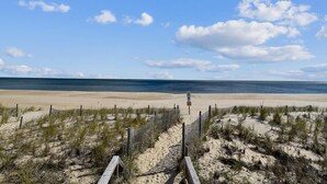 A beach with a wooden boardwalk leading to the water, a sandy beach, and a clear sky. - Walk to Beach | 4BR Beach House w/ Decks + Kitchen (Tower Shores)
