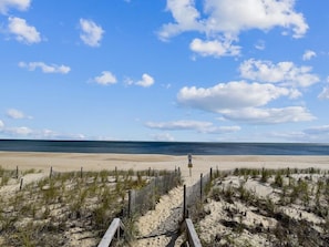 A beach with a wooden boardwalk leading to the water, a sandy beach, and a clear sky. - Walk to Beach | 4BR Beach House w/ Decks + Kitchen (Tower Shores)