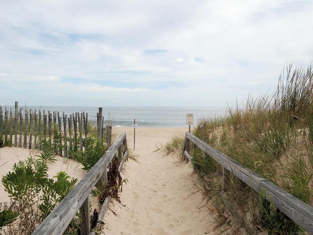 A sandy beach path with wooden railings and a signpost.