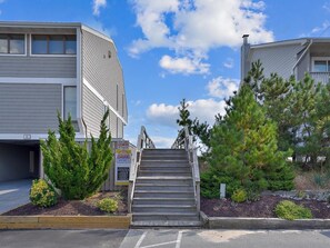 A building with a staircase leading to a parking area, surrounded by greenery and a clear sky. - Walk to Beach | 4BR Beach House w/ Decks + Kitchen (Tower Shores)